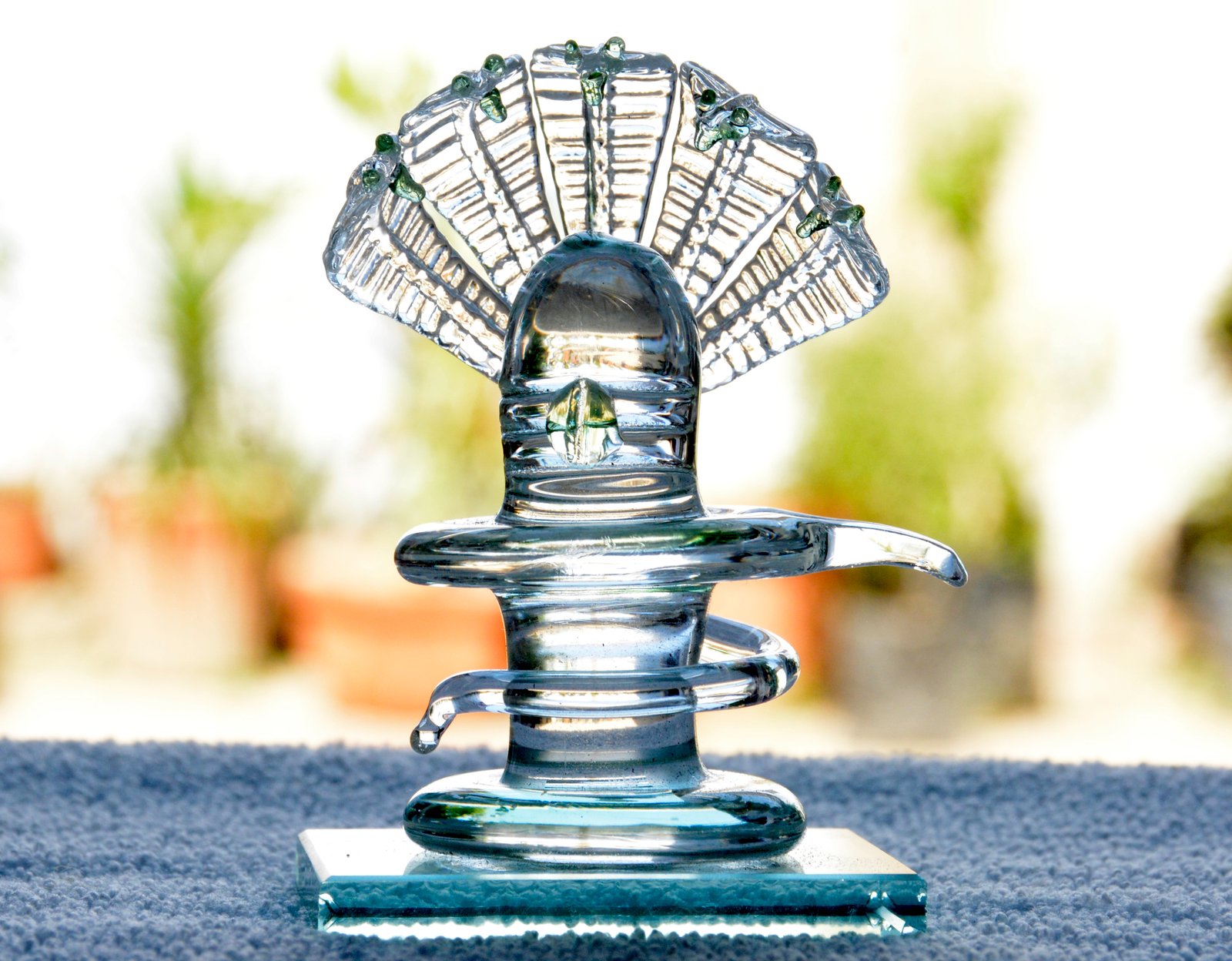 A clear glass Shivling with subtle green accents, presented on a glass base, showcasing a modern, artistic interpretation of the traditional Hindu symbol.