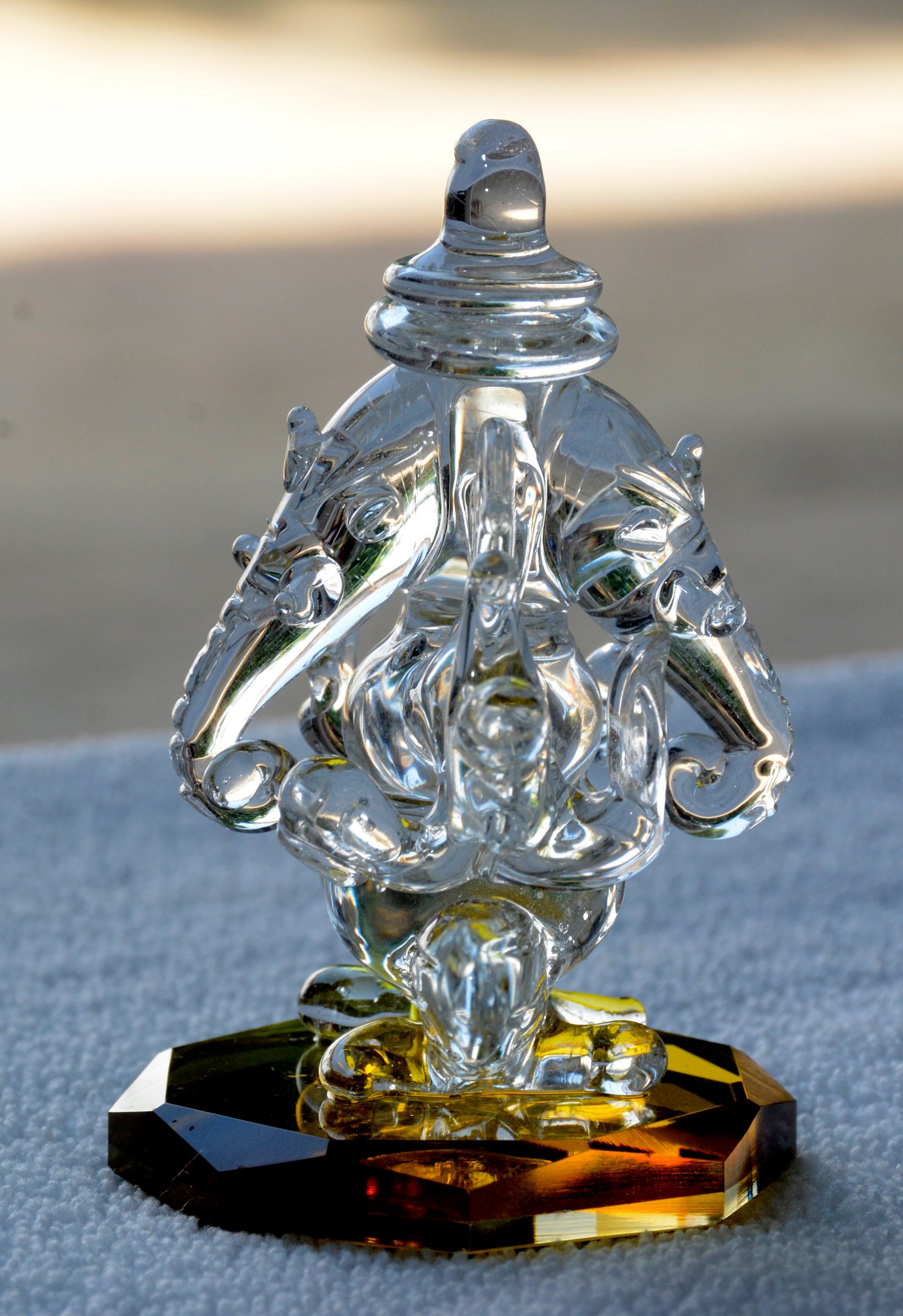 A clear glass representation of Lord Ganesha, featuring a unique double-sided design and resting on a faceted, jewel-toned base.