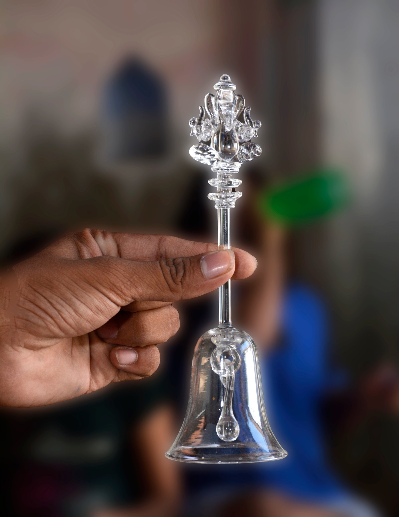 A delicate, clear glass bell featuring a representation of Lord Ganesha JI at its top.