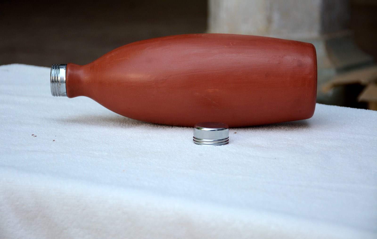 A rustic, terracotta clay water bottle with a detachable metal screw cap.