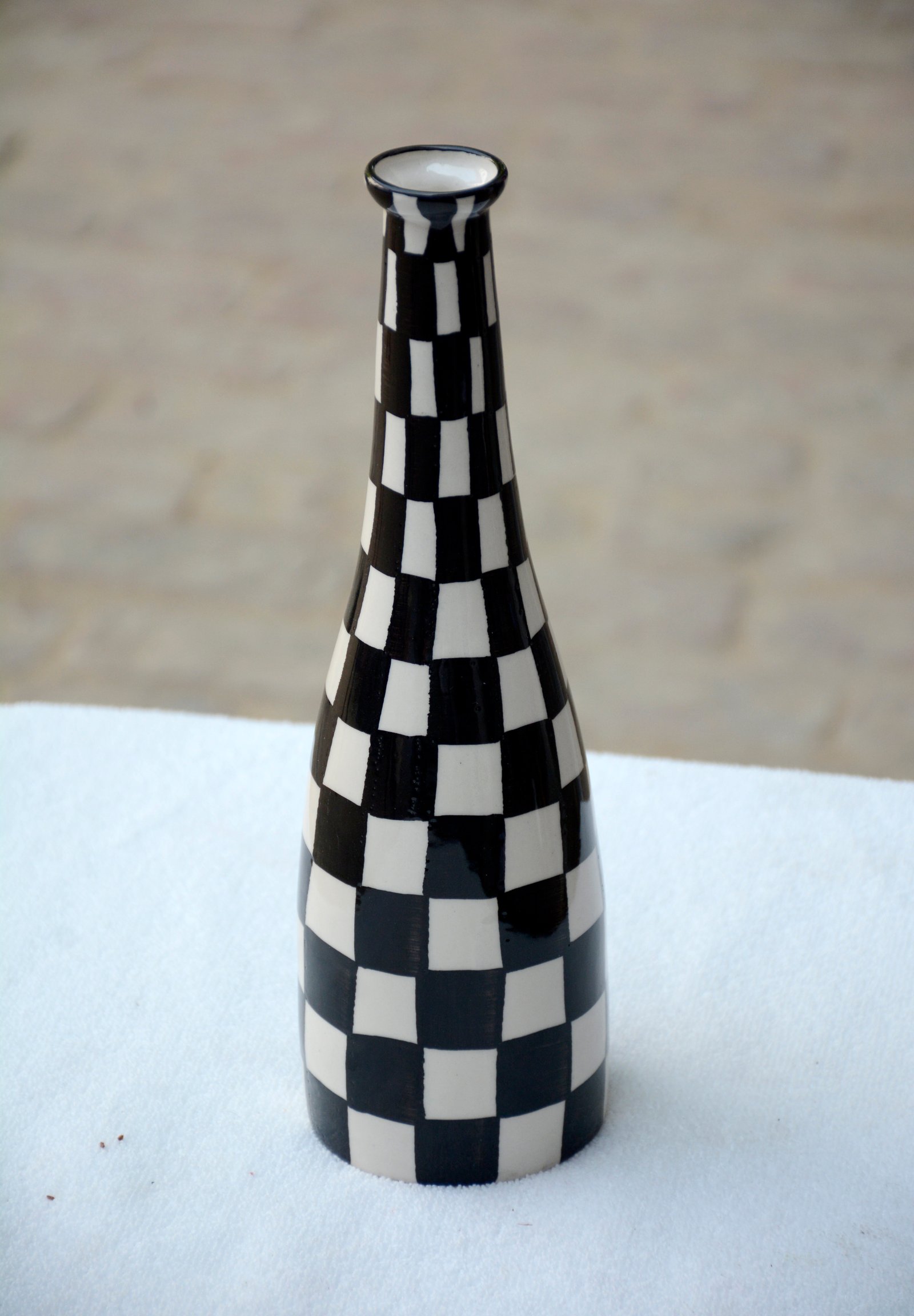 A whimsical, hand-painted ceramic vase featuring a bold black and white checkerboard pattern.
