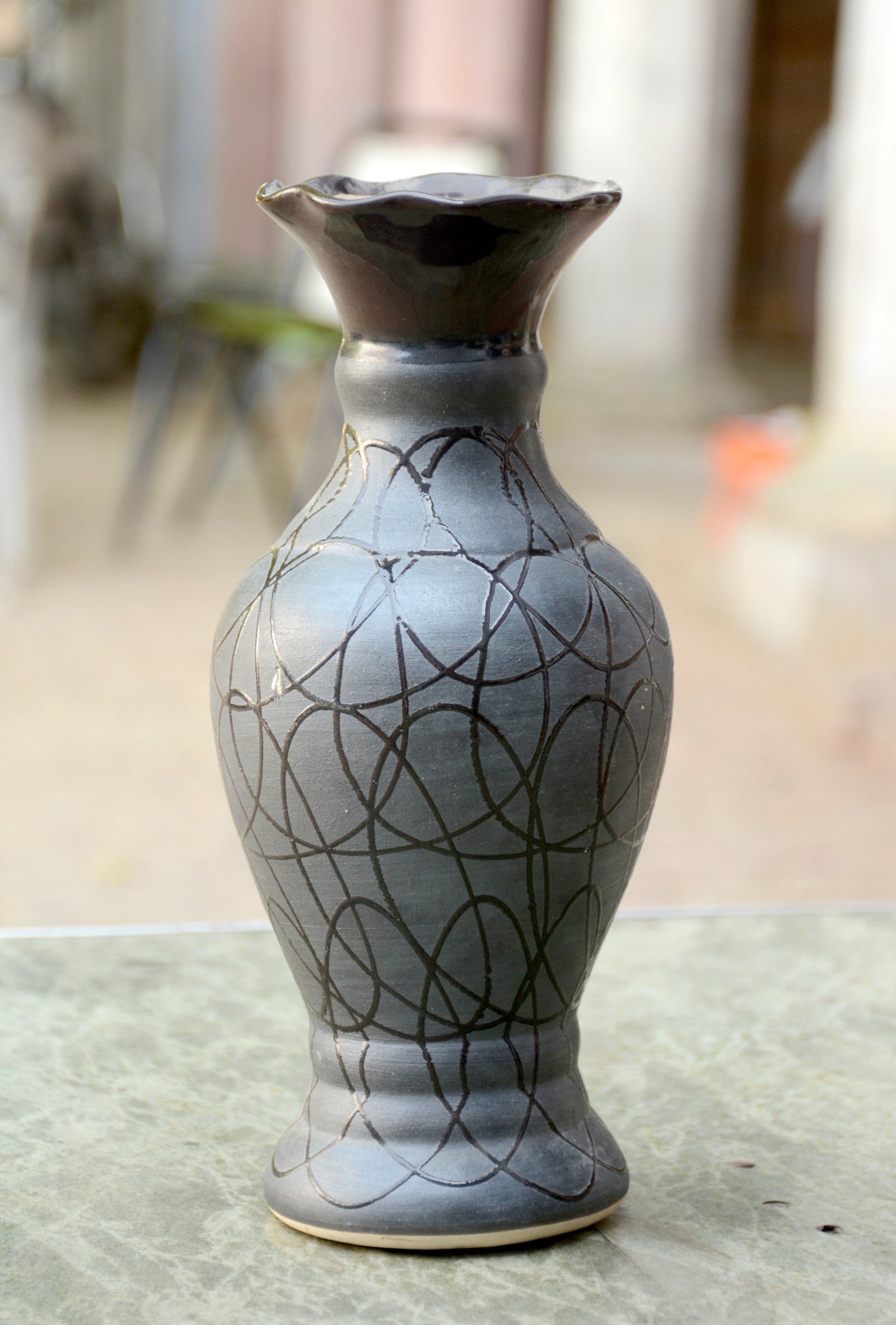 A classic, elegantly shaped ceramic vase with a dark, muted color palette and a distinctive, hand-drawn geometric pattern.