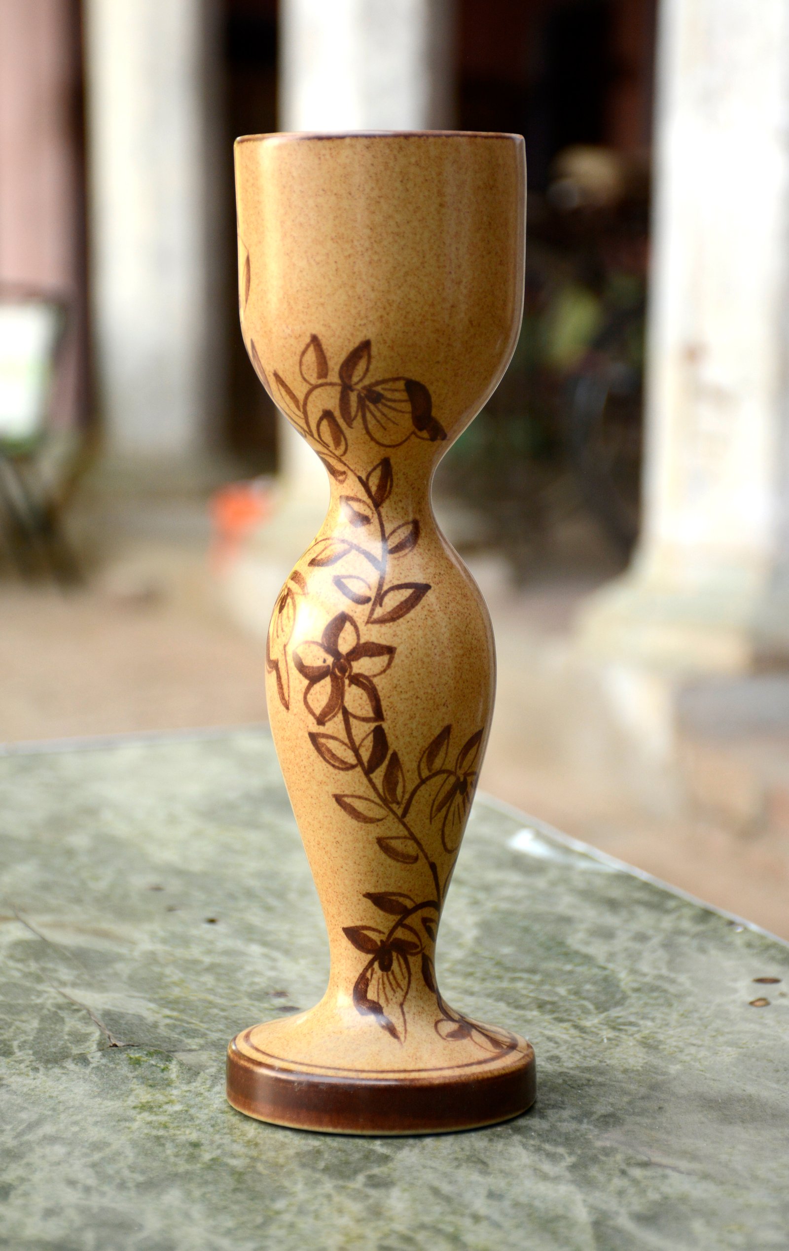 A unique, hourglass-shaped ceramic vase featuring a warm, speckled finish and hand-painted floral motifs.